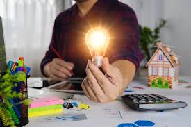 Person holding illuminated lightbulb sitting at a desk with a calculator and other office supplies strewn about